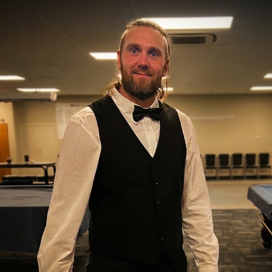 Wiggy stands in a snooker room wearing his waistcoat and bowtie.